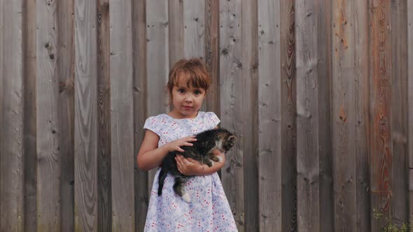 Portrait of Small Happy Pretty Girl Standing in the Farm in Cute Dress with Flowers and Hugging Cute