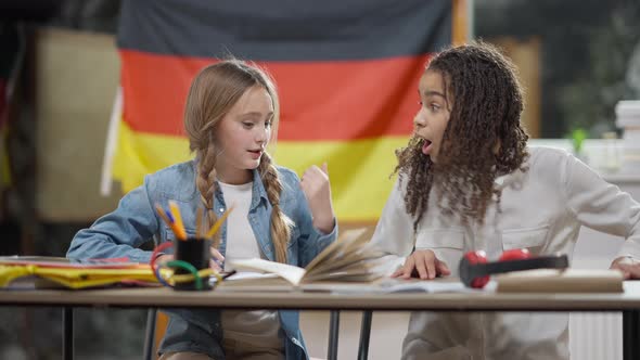 Smart Genius Caucasian Schoolgirl Writing in Workbook and Declaiming As African American Classmate