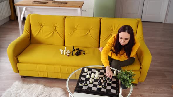 Young Woman Sitting on Yellow Sofa and Playing Chess in Room