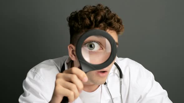 Medical Intern surprised, who is looking at the camera through a magnifying glass