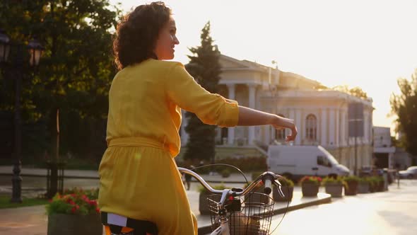 Back View of a Beautiful Woman Riding a Citybike with a Basket and Flowers in the City Center