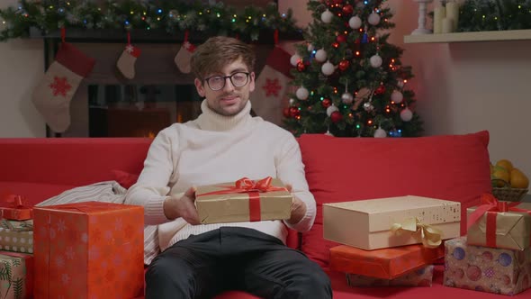 Handsome man looking at camera sitting on sofa with gift boxes.