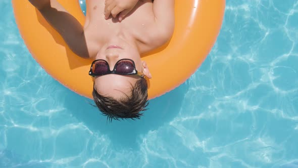 Topdown view Boy with Smartphone, Relaxing on a Floater in Swimming pool, Summer concept