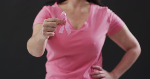 Mid section of woman holding a pink ribbon against black background