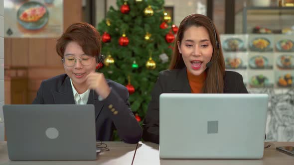 Two businesswoman using microphone headphone headset and laptop for online meeting while in cafe