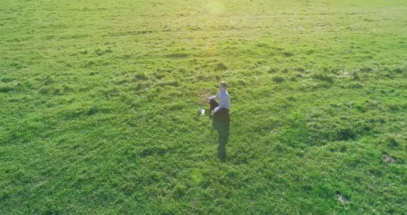 Low Orbital Flight Around Man on Green Grass with Notebook Pad at Yellow Rural Field.