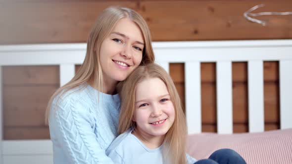 Medium Closeup Portrait of Happy Young Woman and Cute Little Daughter Hugging and Looking at Camera