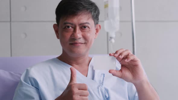 Elderly Asian male patient holding life insurance card during hospitalization.