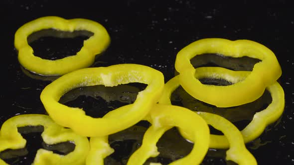 Rings of Yellow Bell Pepper Falling on a Wet Black Surface