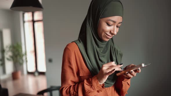 Happy Muslim woman typing by phone