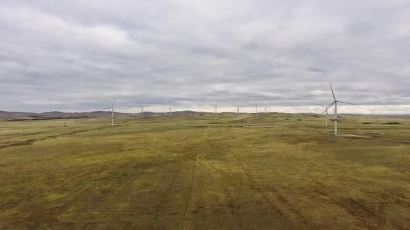 Motion the Blades of a Large Wind Turbine in a Field Against a Background of Orange Sunset on the