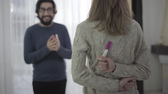 Back View of Young Caucasian Woman Holding Pregnancy Test with Two Stripes Behind Her Back