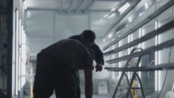 Two Male Painters Prepare Steel Metal Elements for Painting By Fixing Them on Suspensions