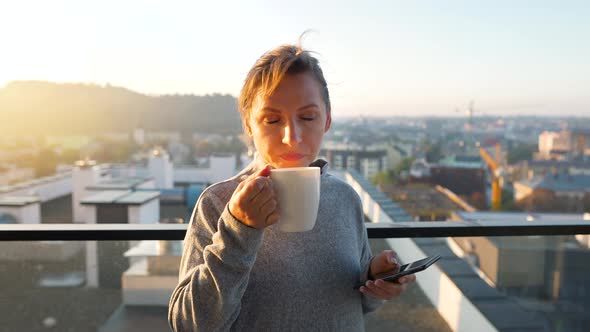 Woman Starts Her Day with a Cup of Tea or Coffee and Checking Emails in Her Smartphone on the