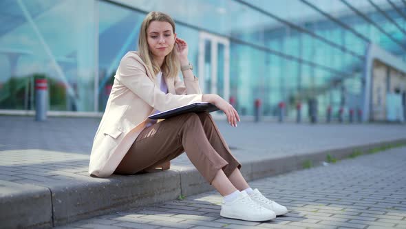 longing young woman sitting alone on street sidewalk on urban background 