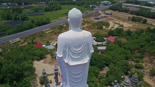 Drone Flies From White Buddha Statue Back Around Against Road