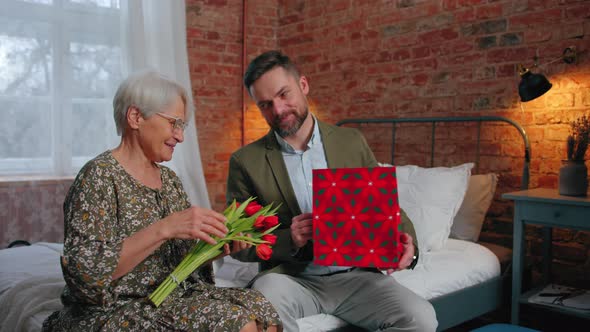 Middleaged Entrepreneur Celebrating His Mother's Birthday and Giving Her a Bouquet of Red Tulips and