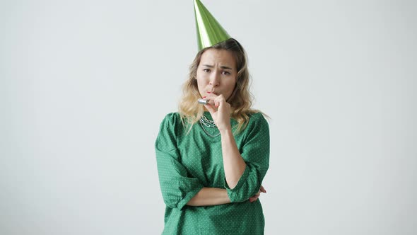 Portrait of Miserable Young Woman Wearing Party Hat Blowing Horn with Sad and Disappointed Face