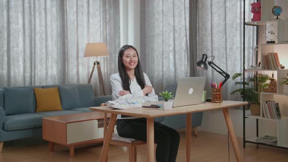 Female Footwear Designer Smiling And Crossing Her Arms To The Camera While Working On A Laptop