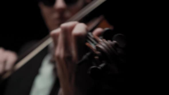 Young Caucasian Male in Black Suit and Glasses Plays Violin on Dark Background