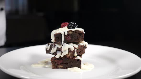 Stack of Brownies Dessert Being Decorated with Berries on White Plate. Falling Berries in Slow