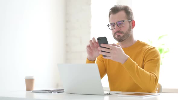 Man Using Smartphone While Using Laptop in Office