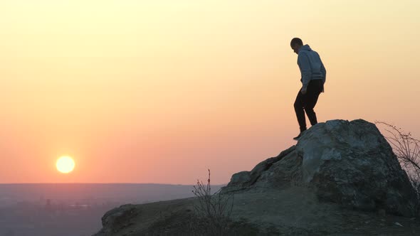 Silhouette of a Man Hiker Climbing Alone on Big Stone at Sunset in Mountains