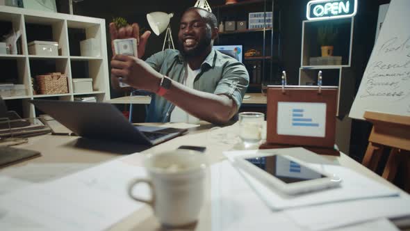 Cheerful African Businessman Stacking Money at Modern Workplace in Slow Motion.