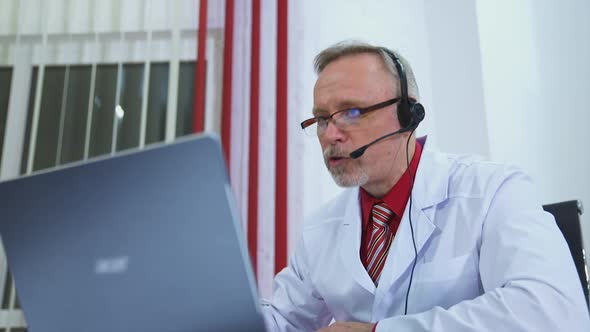 Doctor in surgery office with headphones in front of his laptop. Telemedicine concept