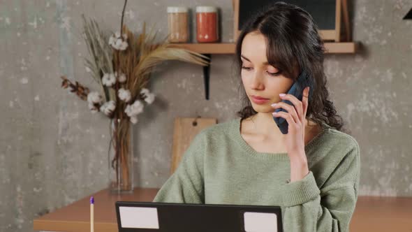 Girl Sitting at Laptop in Her Living Room Talking on Phone and Writing Notes