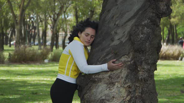 Good looking young brunette woman closing her eyes while hugging a tree in Palermo Woods.