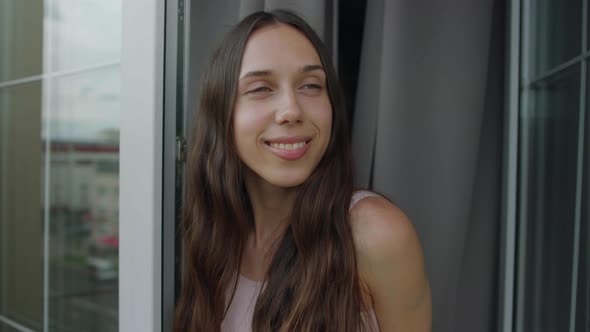 A Young Woman in Pajamas Opens the Curtains in a Good Mood