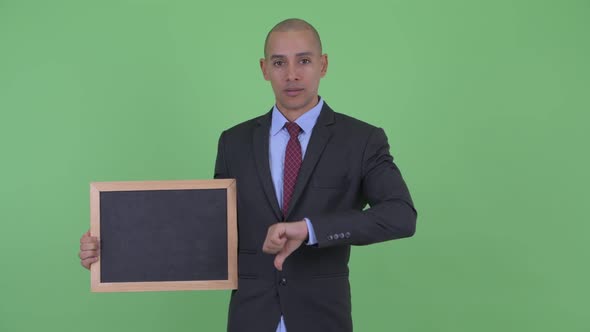 Stressed Bald Multi Ethnic Businessman Holding Blackboard and Giving Thumbs Down