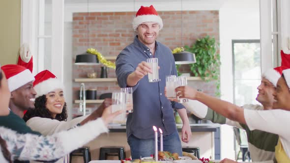 Happy group of diverse friends in santa hats celebrating meal, toasting with juice at christmas time