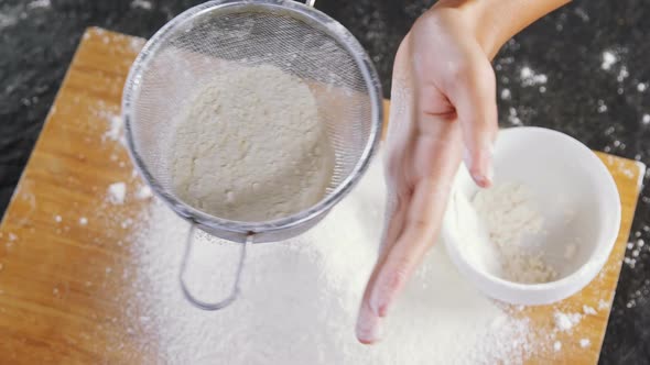 Woman sieving flour from the bowl on the wooden board 4k