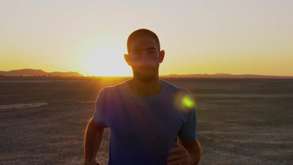 Athletic man working out with battle ropes on a dry lake at sunset