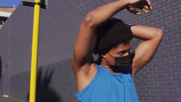 Fit african american man exercising in city wearing face mask,stretching in the street