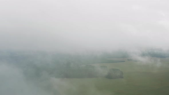 Aerial Top View Drone Flies Through Heavenly Fluffy Rain Clouds Rolling Over Green Forest and Field