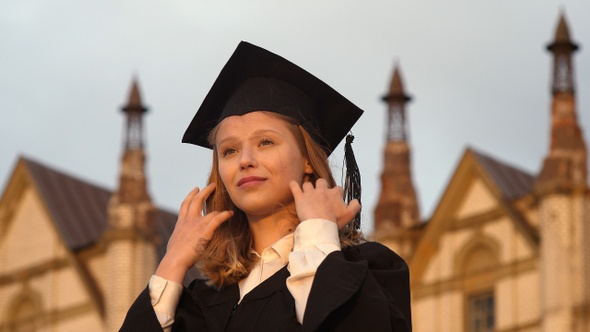 Beautiful young woman graduate straightens her hair and a cap.