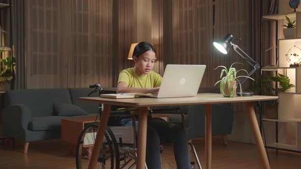 Asian Kid Girl Sitting In A Wheelchair While Using Laptop Computer At Home