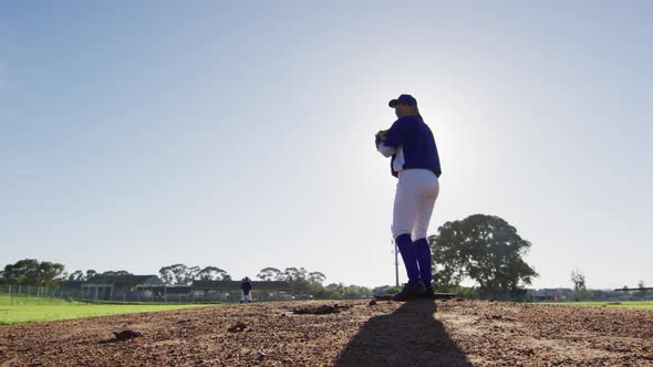 Caucasian female baseball player wearing glasses pitching ball on sunny baseball field