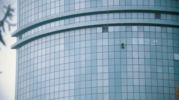A Man Worker Hanging on Ropes By the Exterior Windows of a Skyscraper - Industrial Alpinism