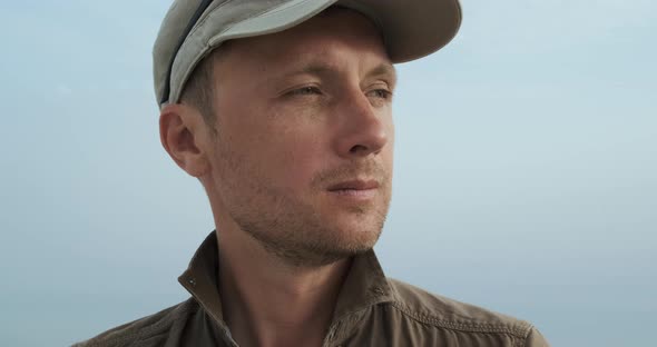Portrait of Man Traveler in Cap and Khaki Shirt Against Background of Blue Sky
