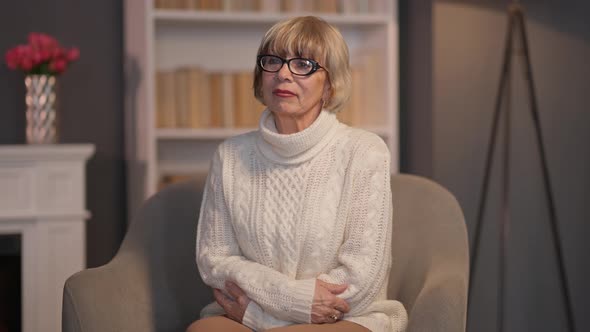 Thoughtful Wealthy Senior Woman Sitting on Armchair in Living Room Looking Away