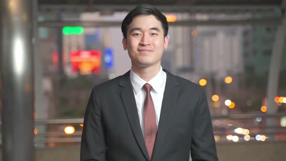 Portrait shot of Asian young handsome businessman taking off or removing face mask outdoors in city.