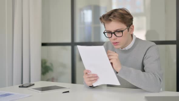 Young Man Reading Documents While Sitting in Modern Office