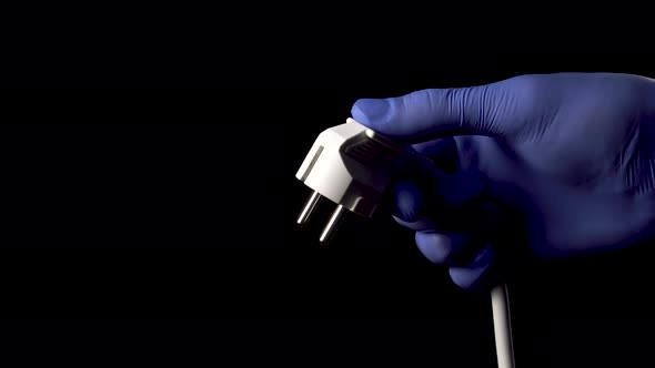 Hand in a protective medical glove holds an electrical plug