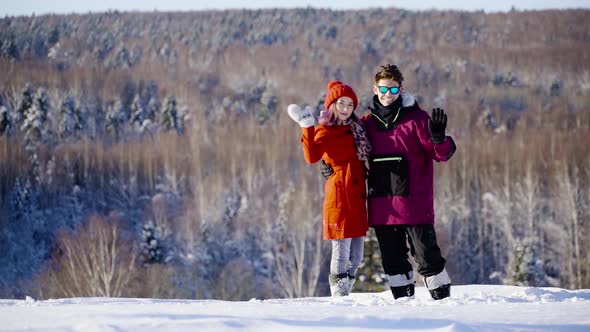 Happy Coulple Waving Hands to Camera in Mountain Ski Resort at Sunny Day