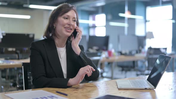 Cheerful Middle Aged Businesswoman Talking on Smartphone at Work