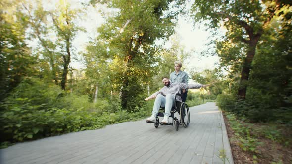 Disabled Person Man is Fooling Around with His Girlfriend in Park Riding Wheelchair and Spreading